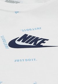 Άσπρο βαμβακερό μπλουζάκι με μεγάλο ναυτικό λογότυπο Nike και κείμενο «JUST DO IT» σε ανοιχτό μπλε γύρω από το σχέδιο, με στρογγυλή λαιμόκοψη και λεία υφή.