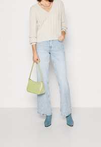 Pull en maille côtelée beige clair avec un col en V, associé à un jean large bleu clair. Un sac à main vert texturé et des bottines bleues complètent le look.