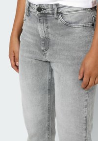 Jeans de denim gris con un corte clásico, que incluyen bolsillos frontales, un cierre de botón y un desvanecimiento sutil en la tela.
