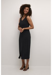 Dark grey, sleeveless midi dress with a v-neck and ruched detail at the front. Features a side slit for ease of movement. Worn with black heels.