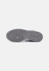 Grå sneaker tå med teksturert gummi, sirkel- og linjemønstre, med et sentralt logo. Glatte kanter og en flat profil.