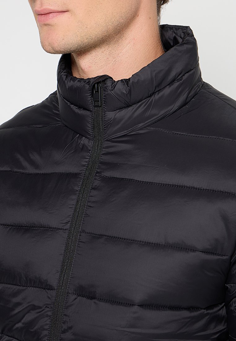 Chaqueta de plumas negra con cuello alto, diseño acolchado, cremallera frontal y textura suave y brillante. Sin logotipos ni patrones visibles.