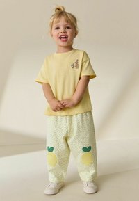 Gul bomulls-T-shirt med broderad kanin, kombinerad med ljusgula byxor med citronapplikationer och gröna lövdetaljer. Vita skor.