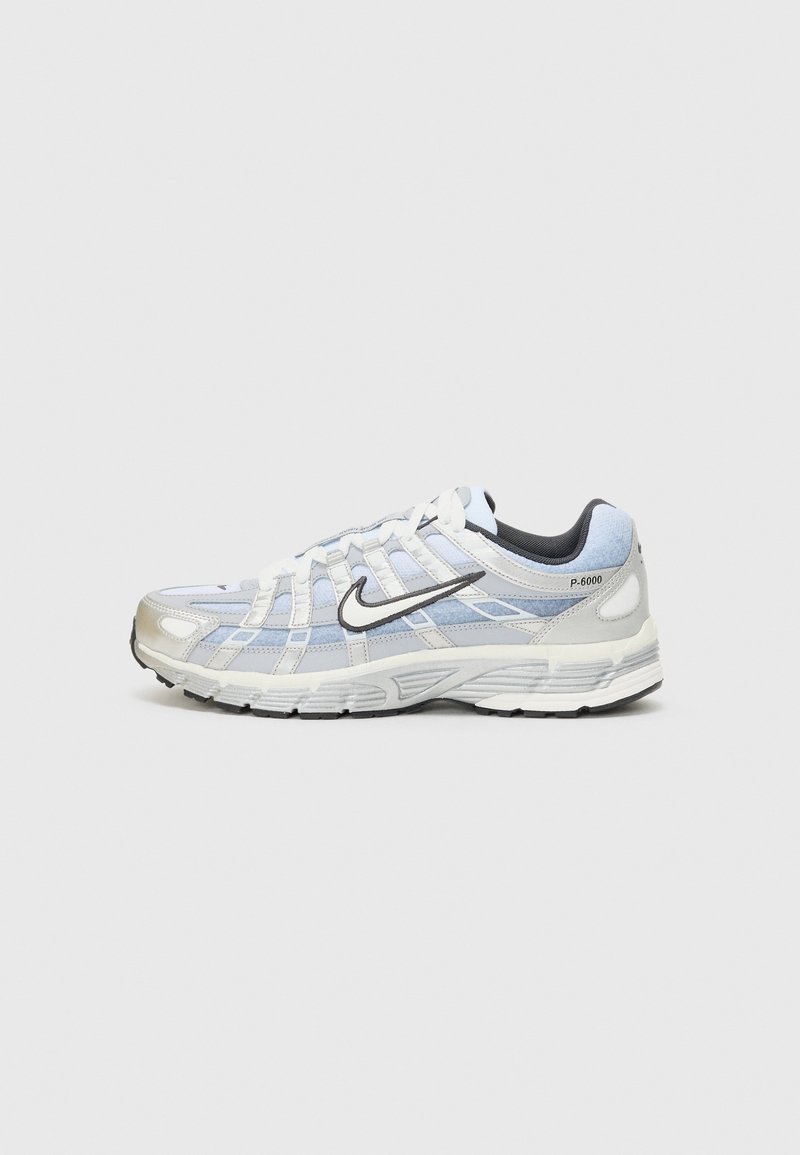 Baskets Nike P-6000 blanches et bleu clair avec logo swoosh noir, lacets blancs et semelle grise sur un fond gris uni.