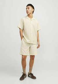 Camisa corta de color beige claro y pantalones cortos a juego, hechos de una tela texturizada, con sutiles rayas verticales, combinados con zapatillas marrones.
