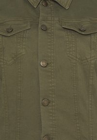 Chaqueta vaquera verde oliva de frente con botones de presión metálicos y dos bolsillos de solapa en el pecho con cierre de botón.