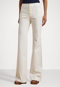 Witte katoenen wijde broek met een vijfknoopssluiting aan de voorkant, twee opgestikte zakken en een zachte textuur; gecombineerd met bruine platform sandalen.