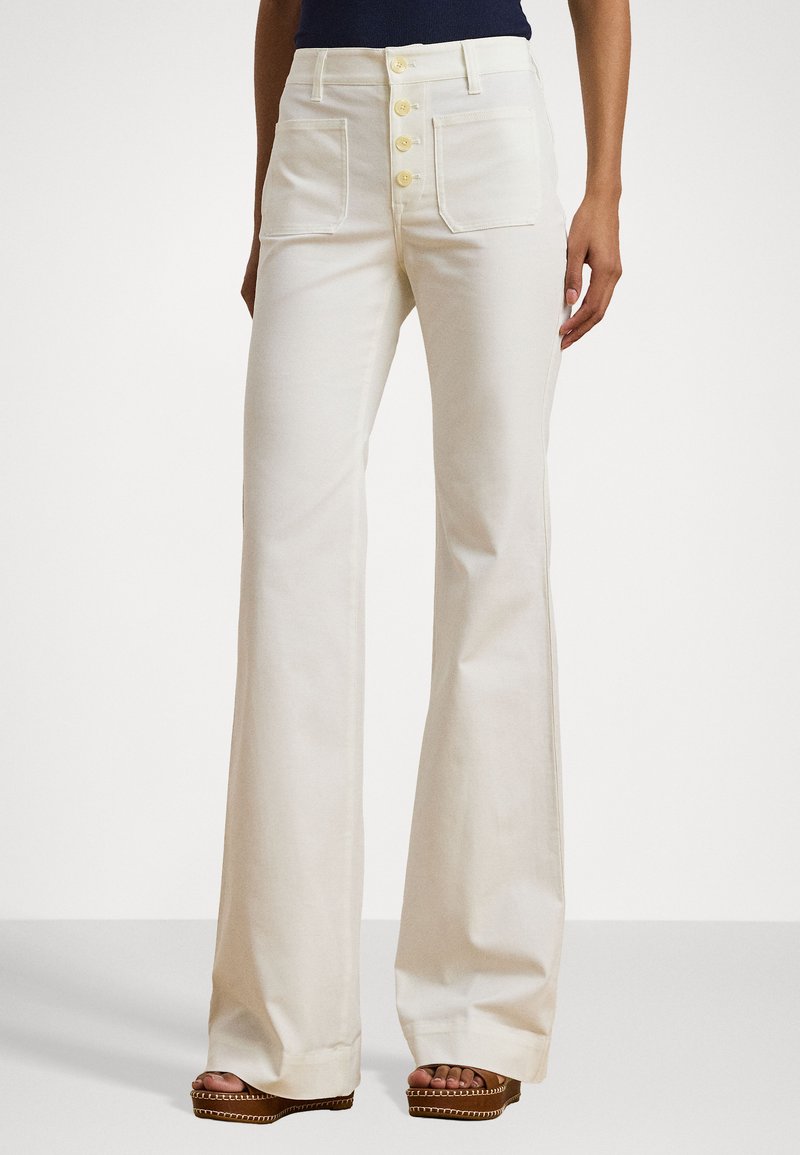 Witte katoenen wijde broek met een vijfknoopssluiting aan de voorkant, twee opgestikte zakken en een zachte textuur; gecombineerd met bruine platform sandalen.