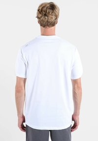 T-shirt blanc en coton à manches courtes, avec une texture lisse et une étiquette logo sur le haut du dos. L'ourlet est légèrement incurvé.