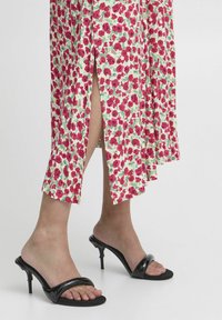 Floral print dress featuring red and green patterns, with side slits. Paired with black heeled sandals, showcasing a smooth, glossy finish.