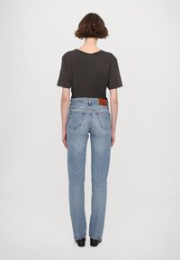 Juodas marškinėliai su trumpomis rankovėmis, derinami su šviesiai mėlynomis tiesiomis džinsomis. Šiek tiek blukinta džinsinė tekstūra, su užpakaliniais kišenėmis ir odiniu ženkleliu.