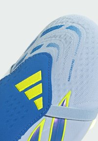 Gros plan sur une chaussure de football blanche et bleue avec un logo Adidas jaune et le texte "NANOSTRIKE PRO" sur la surface supérieure texturée.