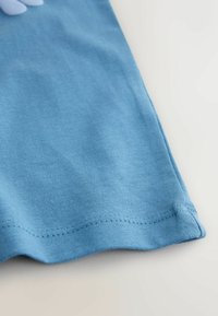 Zils kokvilnas audums ar ribotu faktūru, ar gludu apmali un kārtīgu šuvi, krekla malas tuvplāns.