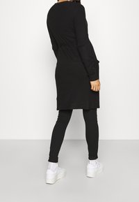 Black long-sleeve dress with a belted waist, featuring a knee-length cut and side pockets, paired with black leggings and white sneakers.