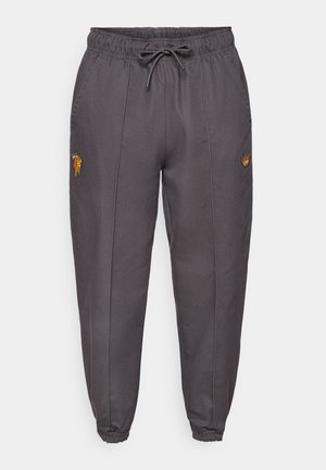 Pantalon de jogging gris foncé en tissu lisse, avec une ceinture élastique, un cordon de serrage et de subtils logos brodés sur les côtés.
