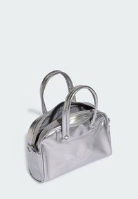 Srebrna metaliczna torebka na dualnych uchwytach, z zamknięciem na zamek i wytłoczonym logo z przodu. Gładka tekstura o ustrukturalizowanym kształcie.