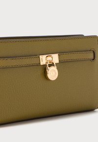 Portafoglio in pelle verde oliva con una finitura testurizzata, hardware con chiusura in tono oro e un accento con logo rotondo. Presenta un design elegante e rettangolare.