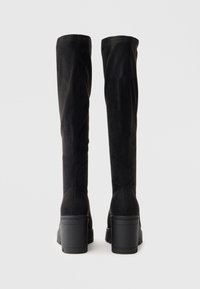 Melnas virsceļgala zābakus, kas izgatavoti no mīksta zamša, ar taisnu dizainu, platā bloka papēdi un minimālistiskām šuvēm aizmugurē.