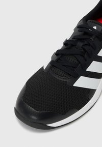 Black athletic shoe with a mesh upper, featuring white accents and laces. The toe has a glossy finish, and the sole is textured for grip.
