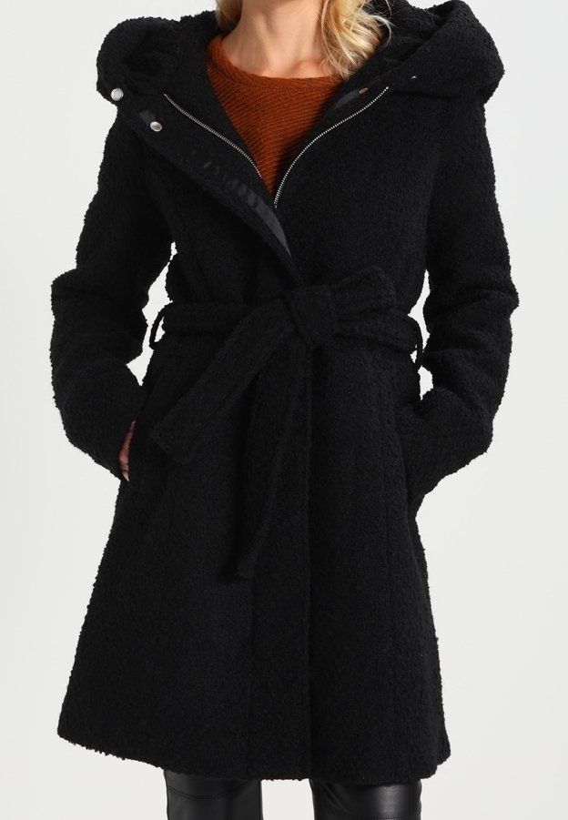 Manteau mi-long noir texturé avec capuche, taille ceinturée et fermeture éclair, porté sur un pull couleur rouille.