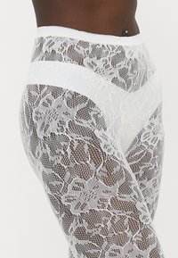 Vita spetsleggings med ett blommönster och en slät midjeband. Strukturen är genomskinlig med en nätliknande design överallt.