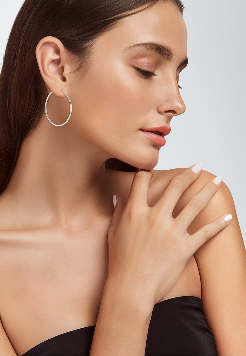 Silberne Creolen sichtbar, glatte Oberfläche, kreisförmiges Design. Ein Model mit langen Haaren posiert vor einem neutralen Hintergrund. Hände ruhen auf der Schulter.
