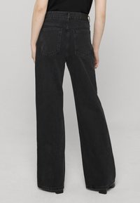 Jean noir à jambes larges en denim. Caractérisé par une taille haute, des passants pour ceinture et deux poches arrière. Le tissu présente une texture subtile.