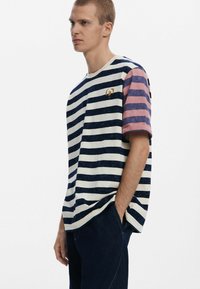 Cotton t-shirt featuring navy and white horizontal stripes, short pink-striped sleeves, and a small golden logo on the chest.