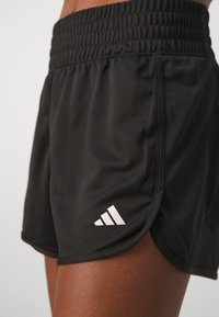Black athletic shorts with an elastic waistband, featuring a white Adidas logo on the lower left side and a smooth, lightweight fabric.