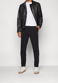 Zwarte leren motorjack, witte t-shirt met ronde hals, zwarte slim-fit broek en witte sneakers met beige accenten. Minimalistisch ontwerp en strakke textuur.