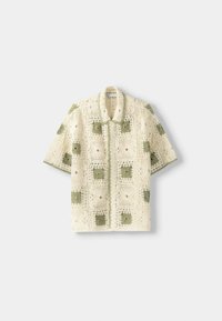 Camiseta de manga corta de crochet en color crema con patrones de cuadros verdes, con cuello y textura de tejido abierto. Cierre frontal con botones.