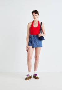 Röd halterneck-baddräkt tillsammans med en jeanskjol med en framsläp, och leopardmönstrade skor med lila accenter och vita strumpor.