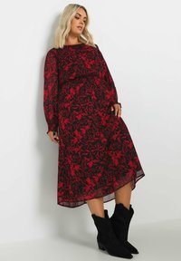 Svart klänning med röd blommönster, långa ärmar, medellängd till vaden, lättviktig tyg och matchad med svarta cowboyboots.