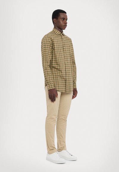 Long-sleeve plaid shirt in brown and green, button-down collar, paired with beige slim fit pants and white sneakers. Smooth cotton texture.