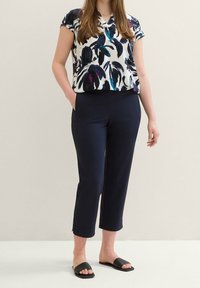 Blusa floreale in bianco, blu navy e teal; pantaloni cropped blu navy con tasche; sandali slide neri; tessuto morbido, vestibilità comoda, maniche corte.