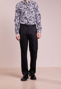 Black and white floral patterned long-sleeve shirt paired with tailored black trousers and shiny black shoes, standing on a neutral background.