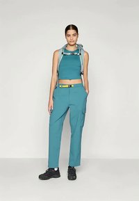 Tīrā zila apģērba komplekts, kas sastāv no saīsinātā tops un brīvi pieguļošām kravu biksēm ar kabatām. Komplektā iekļauta viegla mugursoma un melnas kurpes.