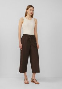 Lichtbeige ribbelige tanktop gecombineerd met donkerbruine cropped broeken met een elastische tailleband. Model draagt platte sandalen met luipaardprint.
