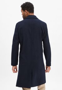 Marineblauer Wollmantel mit Reverskragen, langen Ärmeln und einer taillierten Silhouette mit einem Schlitz hinten. Glatte Textur und klares Design.
