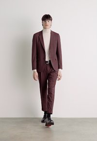 Burgundy suit with a fitted silhouette, paired with a cream turtleneck. Accessories include glasses and black shoes with red accents.