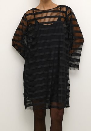 Schwarzes Kleid mit einem plissierten, durchsichtigen Design und horizontalen Streifen. Lange Ärmel und ein runder Halsauschnitt. Unterkleid sichtbar.