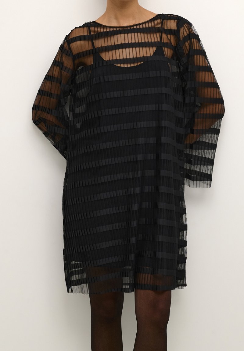 Robe noire avec un design plissé et transparent à rayures horizontales. Manches longues et encolure arrondie. Sous-vêtement visible.