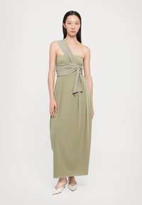 Rochie maxi de culoare verde măsliniu, cu un design pe un umăr și un detaliu legat la talie. Material neted cu o siluetă fluidă.