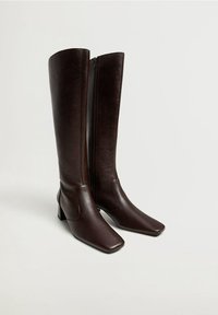 Botas de cuero marrón hasta la rodilla con punta cuadrada, textura suave y cremallera lateral; tacón bloque para mayor estabilidad.