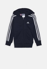 Marineblauwe hoodie met ritssluiting van katoenmix. Heeft witte drie strepen op de mouwen en een logo op de voorkant. Voorzien van kangoeroezakken en een capuchon met trekkoord.