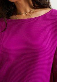 Fuchsiaribbade topp med bred halsringning, prydd med vertikala ränder och avslappnad passform. Lager av silverhalsband framhäver halsringningen.