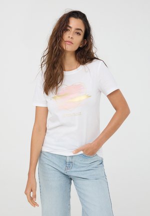 T-shirt di cotone bianco con un design a cuore pastello e dettagli dorati, abbinato a jeans azzurri chiari. Maniche corte e scollatura rotonda.