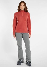 Rød fleece pullover med halv lynlås og lange ærmer, parret med grå skibukser og sorte skistøvler med justerbart udstyr.
