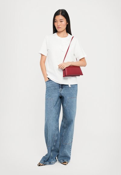 White short-sleeve t-shirt with raised floral design, paired with light blue wide-leg jeans. Accessory: small red leather crossbody bag.