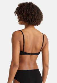 Reggiseno nero senza fili con spalline regolabili e chiusura a gancetto. Tessuto liscio, design minimalista e costruzione della schiena senza cuciture.